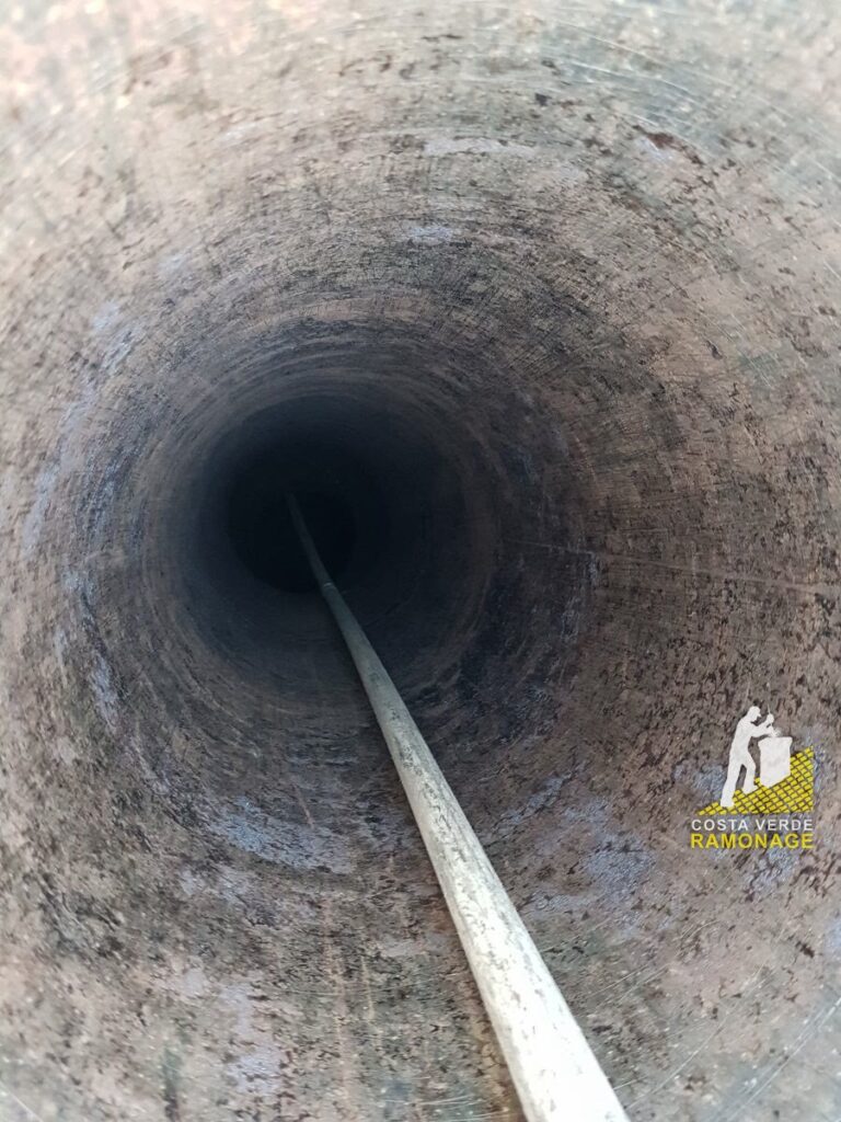 Vue plongeante dans un conduit maçonné avec la canne de ramonage engagée