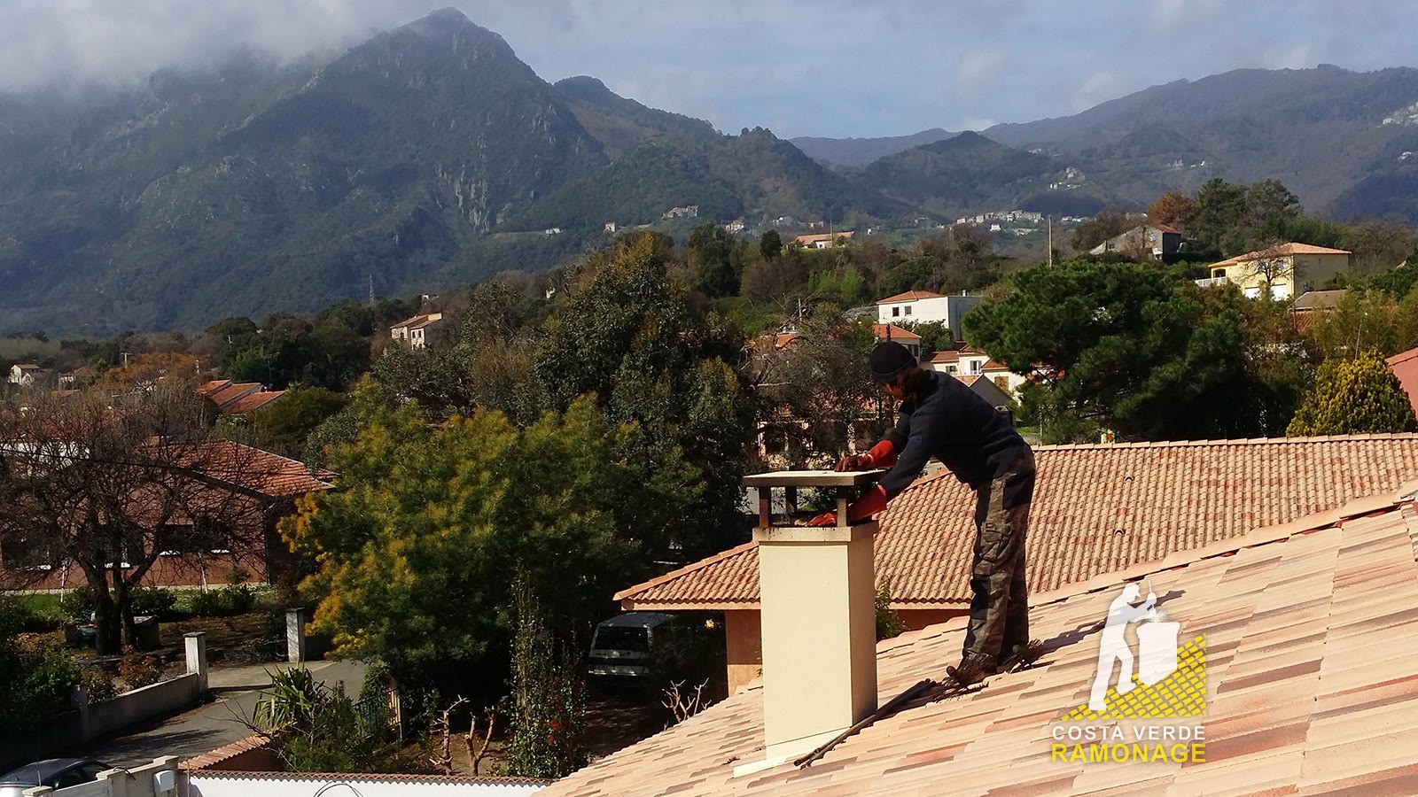 Ramoneur penché sur une souche de cheminée pour inspecter le conduit, montagnes corses en fond