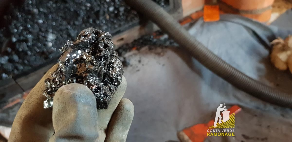 Fragment de bistre noir et brillant tenu dans une main gantée, au-dessus d'une bâche de protection