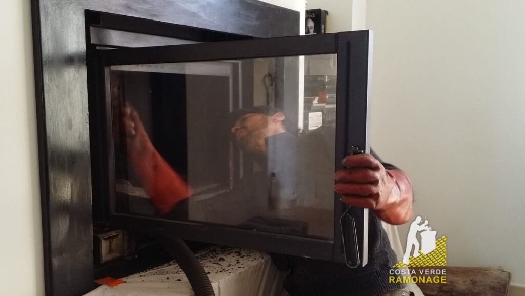 Technicien nettoyant la vitre d'un insert de cheminée à la main