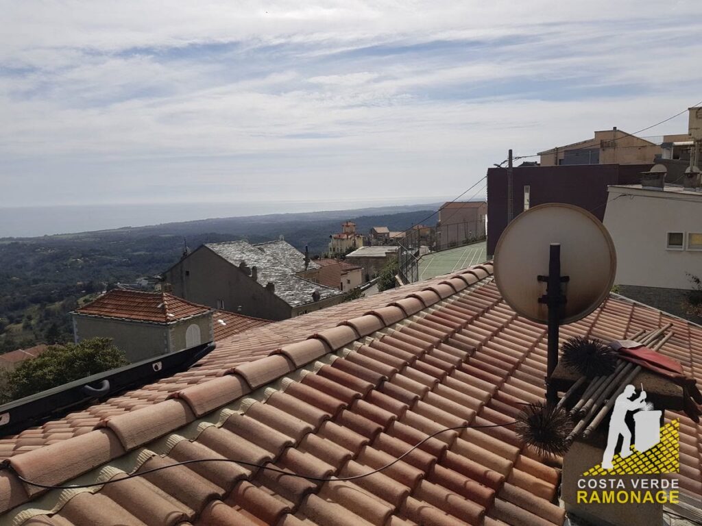 Parabole fixée sur un toit de tuiles, village et mer à l'arrière-plan
