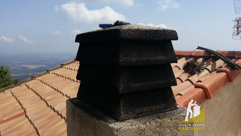 Souche de cheminée coiffée d'un chapeau en béton sur un toit de tuiles rondes, la plaine orientale en contrebas