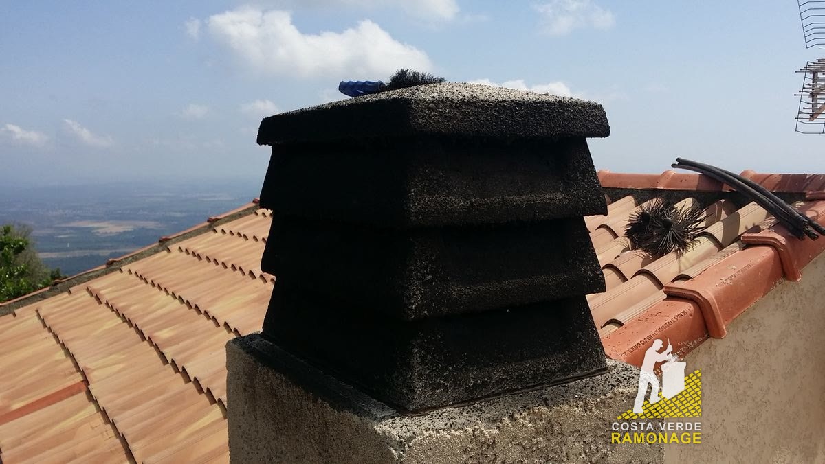 Souche de cheminée coiffée d'un chapeau en béton sur un toit de tuiles rondes, la plaine orientale en contrebas