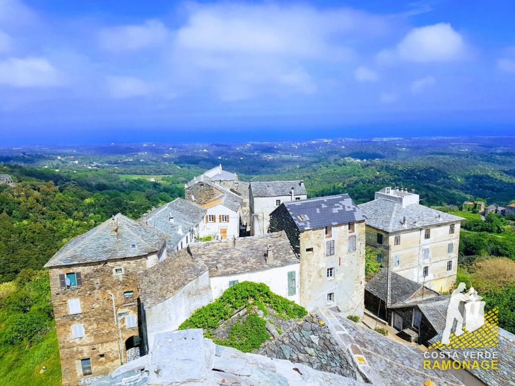 Maisons de pierre et toits de lauzes d'un village de Castagniccia vus depuis une toiture, la plaine et la mer au loin